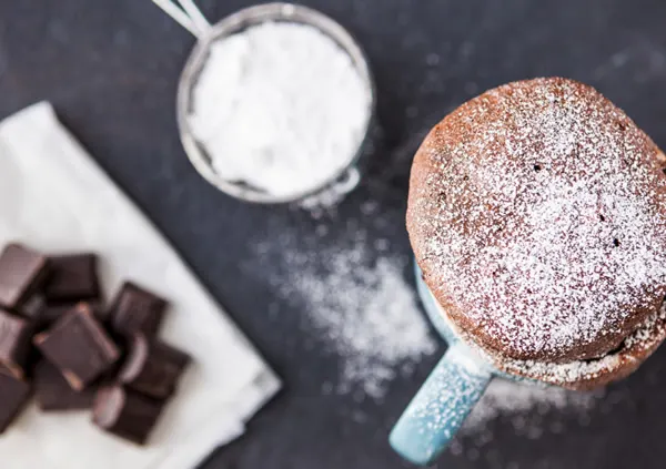 Chocolate mug cake dusted with icing sugar, next to chocolate pieces